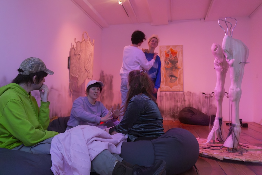 A group of people sitting and standing in an exhibition space talking to each other.